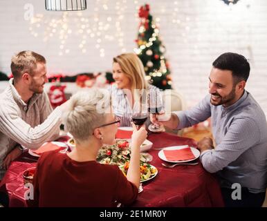 Zwei junge Paare beim weihnachtsessen zusammen. Sitzen an dekorierten Tisch voller Essen und Spaß haben. Stockfoto