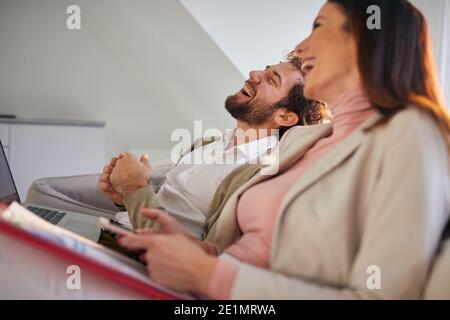 Fröhliches Geschäftsehepaar sitzt nach erfolgreichem Arbeitstag in entspannter Atmosphäre auf der Couch. Geschäftlich, Paar, l Stockfoto