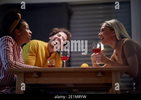 Freunde haben Spaß beim Weintrinken in einer fröhlichen Atmosphäre in der Küche. Abendessen, Freundschaft, zusammen, zu Hause Stockfoto