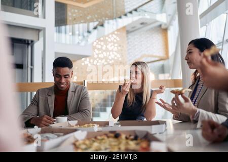 Eine Gruppe von Mitarbeitern essen Pizza in einer Pause in der Firmenkantine in einer angenehmen Atmosphäre. Menschen, Arbeit, Unternehmen, Geschäftskonzept. Stockfoto