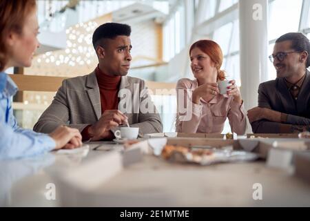 Eine Gruppe von Mitarbeitern in einer Pause genießen Kaffee und Essen in einer fröhlichen Atmosphäre in der Firmenkantine. Menschen, Arbeit, Unternehmen, Geschäftskonzept. Stockfoto