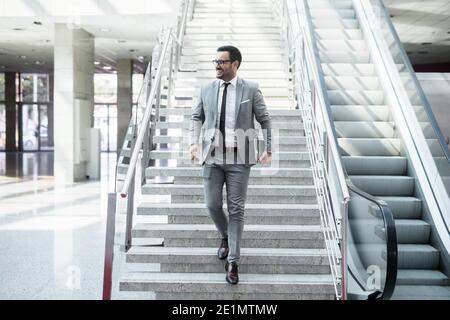 Glücklicher Geschäftsmann, der die Treppe hinuntergeht mit dem Tablet in der Hand. Erfolgreiches Geschäftskonzept. Stockfoto