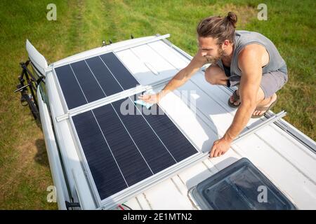 Mann, der ein Solarpanel auf dem Dach eines reinigt Wohnmobil Stockfoto