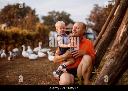 Emotionales Bild des Großvaters, der seinen Enkel im Hinterhof seiner Tierfarm hält. Verbringen Sie einige Zeit zusammen in der Natur und Spaß haben. Stockfoto