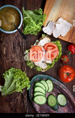 Speck-Sandwich mit frischen Tomaten, Salatblättern, Gurken und Sauce, auf rustikalem Holztisch, niemand Stockfoto