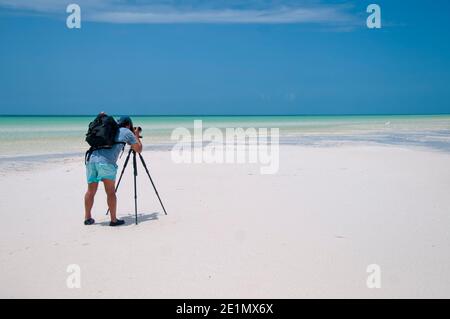 Der Fotograf mit seiner Kamera auf dem Böll macht bei Ebbe Landschaftsaufnahmen auf der Insel Holbox, Mexiko. Im Hintergrund der blaue Himmel an Stockfoto