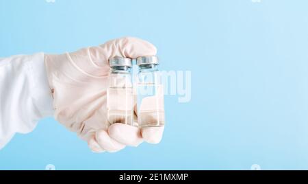 Covid 19-Impfstoff in Flaschen aus Glasfläschchen, Medikamentenflüssigkeit in der Hand des Arztes. Impfungen als Behandlung auf blauem Hintergrund. Covid 19-Immunisierung Stockfoto