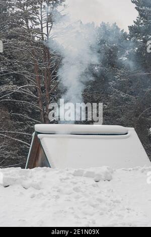 Rauch aus dem Kamin auf dem schneebedeckten Dach des Hauses Stockfoto