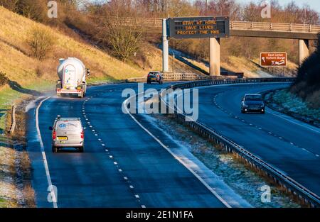 East Lothian, Schottland, Vereinigtes Königreich, 8th. Januar 2021. A1 Lockdown 2 Slogans: Die zweispurige Fahrbahn über der Gantry zeigt die gleichen Covid-19-Nachrichten an wie im April während der ersten schottischen Lockdown, wenn auch in einer etwas anderen Reihenfolge: Stay Home, Save Lives, Protect the NHS. Der Verkehr ist auffälliger als bei der ersten Sperre, als dieser Abschnitt der A1 fast völlig leer war Stockfoto