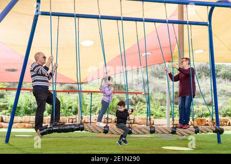 Glückliche Großeltern mit niedlichen Enkeln balancieren zusammen auf einem Seil auf dem Spielplatz. Stockfoto