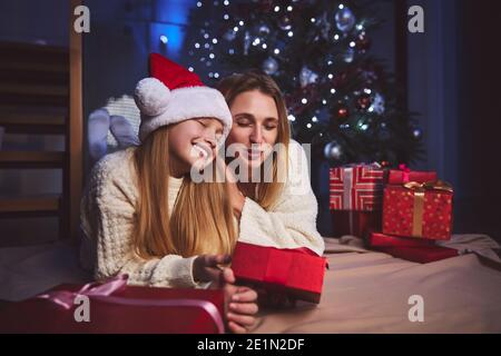 Glückliche Frau umarmt geliebte Tochter unter Weihnachtsbaum Stockfoto