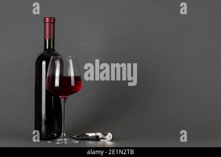 Rotweinflasche, Korkenzieher und Glas auf grauem Hintergrund. Weintrinkkultur Konzept. Leerzeichen für Text. Stockfoto