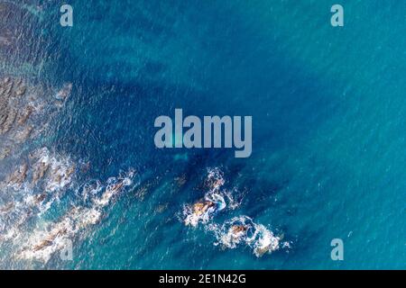 Blick von oben auf das tiefblaue Meer, das mit Felsen zusammenwirkt. Stockfoto