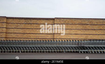 Magdeburg, Deutschland. Dezember 2020. Einkaufswagen stehen in einer langen Reihe vor einer Ziegelmauer. Aufgrund der Corona-Krise darf nur eine begrenzte Anzahl von Kunden in den Supermärkten einkaufen. Deshalb dürfen viele Einkaufswagen nicht benutzt werden. Die Discounter stellen sie normalerweise an einen anderen Ort. Quelle: Stephan Schulz/dpa-Zentralbild/ZB/dpa/Alamy Live News Stockfoto