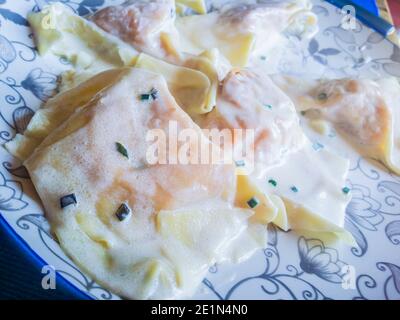 Teller mit Eiernudeln, Ravioli, gefüllt mit Kürbisfüllung und Wurst, gewürzt mit Butter und Salbei, für das Party-Mittagessen Stockfoto