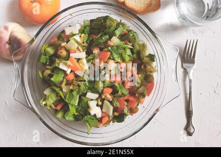 Ein Teller vegetarischen Salats neben Obst, Wasser und Brot auf einem weißen Holztisch. Leerer Kopierbereich für den Inhalt des Editors. Stockfoto