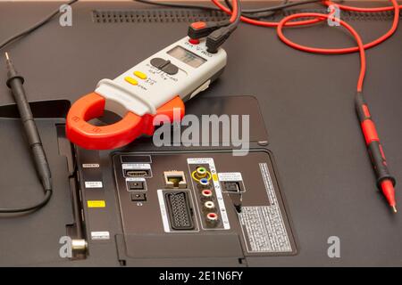 Multimeter und Tastköpfe auf der Rückseite des LCD-Fernsehers. Suchen Sie nach einem defekten Monitor und einer Messung des Stromwiderstands. Nahaufnahme, selektiver Fokus. Stockfoto