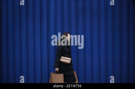 Junge Frau in Winterkleidung mit Papiertüten mit Einkäufen Auf blauem Hintergrund Stockfoto