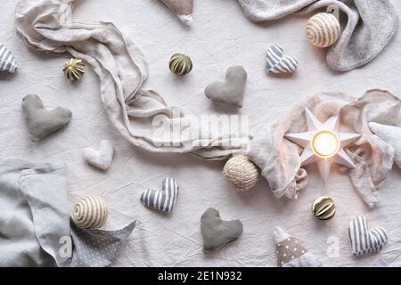 Handgefertigte Leinenherzen und -Bälle auf Leinenhintergrund. Textilhandwerk in neutralen Farben. Frühlingsblumen Zweige. Hand halten weiches Herz Stockfoto