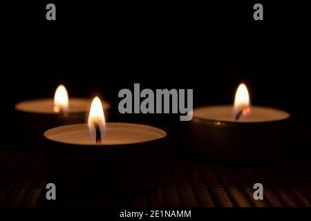 Drei Kerzen im Dunkeln mit Kopierraum. Drei brennende Teelichter Stockfoto