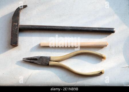 Zwischen Hammer und Zange liegt ein Holzbrett. All dies ist auf schmutzigem weißem Karton. Nahaufnahme. Stockfoto