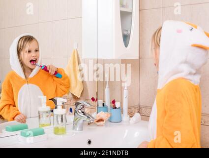 Fünf Jahre altes Mädchen trägt orange Pyjamas Bürsten ihre Zähne Mit elektrischer Zahnbürste im Badezimmer Stockfoto