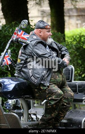 Ein großer Mann aus Bikerleder saß auf seinem Motorrad, und Union Jack-Flaggen flogen vom Lenker Stockfoto