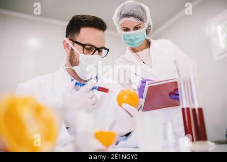 Mitarbeiter in einem Labor, die eine Probe aus Orange mit einer Spritze entnehmen. Stockfoto
