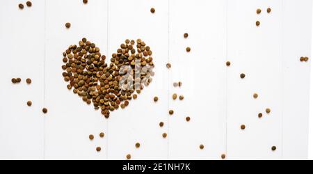 Valentinstag und Liebe zu Haustieren Konzept. Herzförmige Katze trocken kibble Nahrung auf weißem Holzhintergrund verstreut Stockfoto