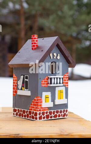 Im Winter steht auf einem Holztisch im Freien ein handbemaltes helles Vogelhaus aus der Nähe. Stockfoto