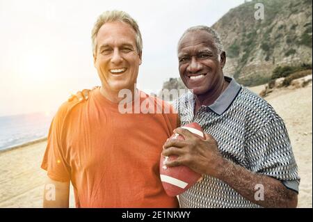 Portrait von zwei multiethnischen reifen männlichen Freunden am Strand Fußball halten Stockfoto