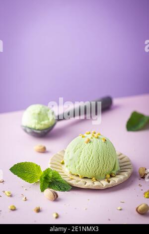 Hausgemachtes Pistazien-Eis mit gehackten Pistazien auf hellrosa und violettem Hintergrund Stockfoto