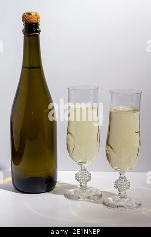 Grüne Flasche mit Champagner innen und zwei Gläser mit Champagner auf weißem Hintergrund. Stockfoto