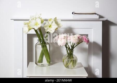 Ein Bouquet von rosa persischen Butterblumen in einer Glasvase und zwei eingewickelte Geschenke auf einem weißen Tisch vor einem falschen weißen Kamin. Bouquet von weißem amary Stockfoto