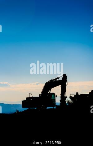 Hinterleuchtete Silhouette eines Baggers auf einem Hügel mit unfokussierten Himmel Hintergrund. Stockfoto