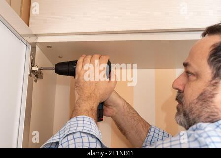 Mann mit einem professionellen Schraubendreher beim Einstellen einer Schranktür Scharnier Stockfoto