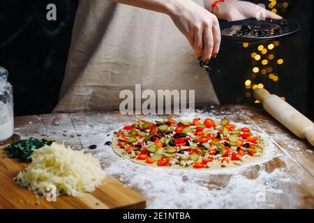 Hausgemachte Pizza Kochen. Frau Hand kochen Gießen Oliven Scheiben auf Teig. Konzept für die Zubereitung von Lebensmitteln unter Quarantäne aufgrund von Epidemien. Stockfoto