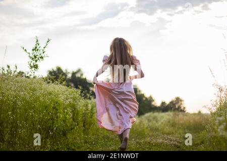 Mädchen läuft über das Feld in einem rosa Kleid Stockfoto