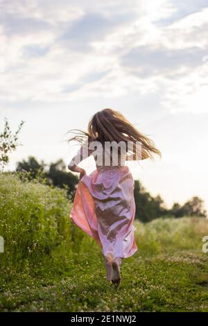 Mädchen läuft über das Feld in einem rosa Kleid Stockfoto