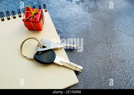 Schlüsselbund, Notizblock und ein kleines Geschenk auf grauem Hintergrund. Stockfoto
