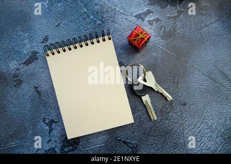 Schlüsselbund, Notizblock und ein kleines Geschenk auf grauem Hintergrund. Stockfoto