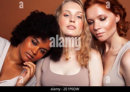 Junge hübsche kaukasische, afro, skandinavische Frau posiert fröhlich zusammen auf braunem Hintergrund, Lifestyle diverse Nationalität Menschen Konzept Stockfoto