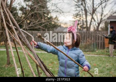 Ein kleines Mädchen in Hasenohren und Jacke baut Fort Mit dem Vater im Hof Stockfoto