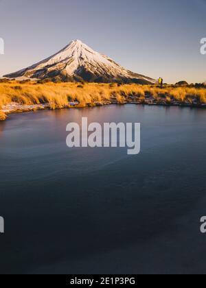 Junges Paar in der Ferne, das den Sonnenuntergang am Mt Taranaki, Neuseeland, genießt Stockfoto