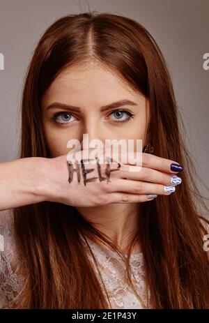 Helft mir! Frau schreit um Hilfe mit gemalter Inschrift auf ihrer Hand. (Angst, Schmerz, Gefahr, Körpersprache, Gesten, Psychologiekonzept) Stockfoto