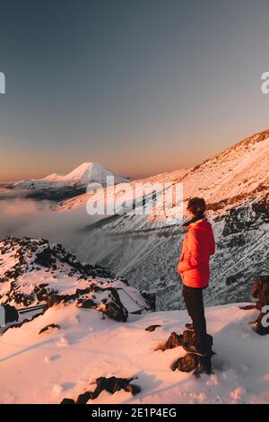 Junge Frau in roter Jacke, die das Skigebiet Mt Ngauruhoe Whakapapa, Tongariro National Park, Neuseeland, beobachtet Stockfoto