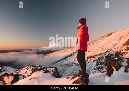 Junge Frau in roter Jacke, die Mt Ngauruhoe, Tongariro National Park, Neuseeland beobachtet Stockfoto