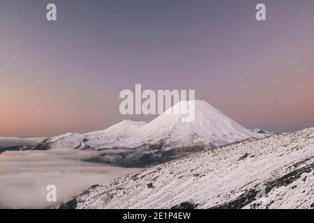 Mt Ngauruhoe über dem Nebel in pastelllila Farben getönt Im Winter im Tongariro National Park Stockfoto