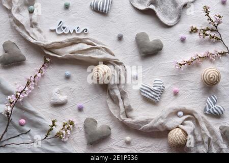 Handgemachte textile Herzen und Bälle auf Leinenhintergrund. Textilhandwerk in neutralen Farben. Pflaumenblütenzweige im Frühling. Rustikale handgemachte Dekor.Hand Stockfoto