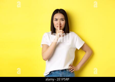 Beauty- und Modekonzept. Wütend und herrisch asiatische Mädchen zu sagen, ruhig zu sein, schimpfen laute Menschen, shushing und Stirnrunzeln an der Kamera, im T-Shirt stehen Stockfoto